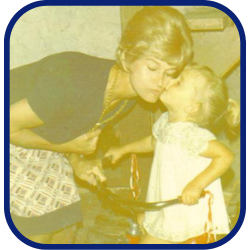 This photograph shows a young girl (Kiersten) holding the handlebars of a tricycle, leaning up to kiss the cheek of her grandmother.